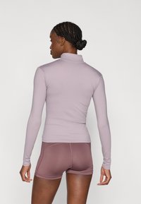 Μπλούζα με μακριά μανίκια και ψεύτικο λαιμό σε απαλό λιλά, σε συνδυασμό με εφαρμοστά σορτς σε μωβ αποχρώσεις. Λεπτή υφή με ελαστικό ύφασμα, ελάχιστες ραφές και αθλητικό σχέδιο.