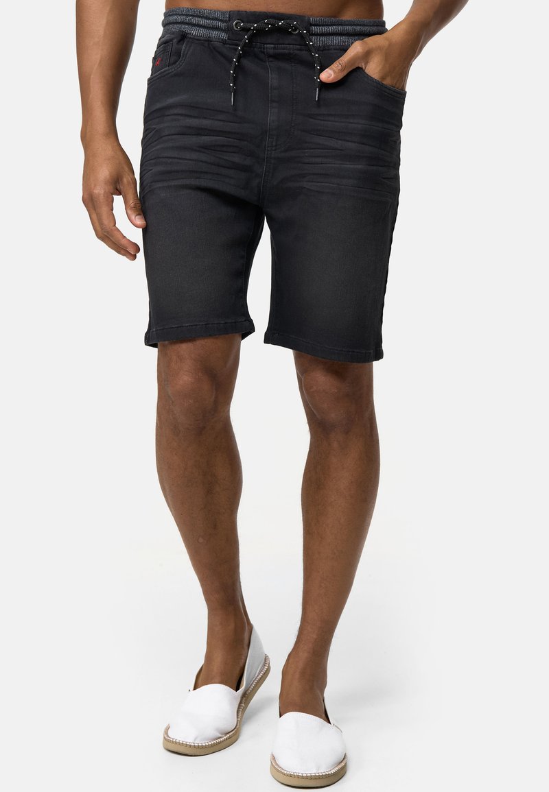 Shorts en denim noir avec taille à cordon de serrage, poches avant, détails texturés subtils et ourlet roulé, associés à des chaussures blanches à enfiler.