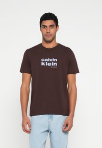Tricou maro din bumbac cu decolteu rotund și mâneci scurte, având inscripționate pe față cu litere albe mari textele „calvin klein” și „New York City”.