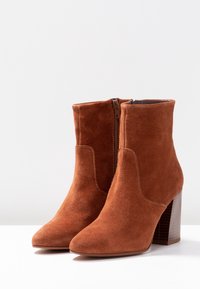 Bottes de cheville en suède marron avec un bout pointu, une fermeture éclair dissimulée et un talon carré texturé. Doublure intérieure lisse.