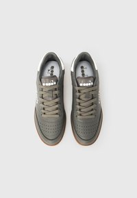 Grå joggesko med perforert detaljering, lisser og såle i gummi. Har hvite aksenter på hælen og logo på tungen.