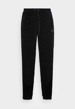 Pantalon de jogging noir texturé avec cordon de serrage, poignets élastiques et poches latérales, présentant un motif en relief subtil et un petit logo sur la cuisse gauche.