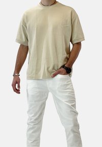 T-shirt in cotone beige con maniche corte e vestibilità comoda, abbinata a pantaloni bianchi. Design semplice, senza motivi o accenti visibili.