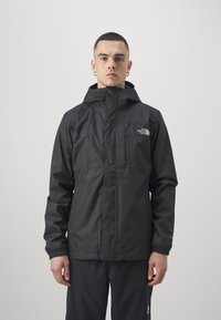 Svart vattentät jacka med huva, med elastiska ärmslut, en zippered framficka och en liten logotyp på övre vänstra bröstet.