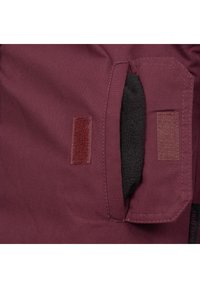 Burgundy jacket fabric with velcro closure, featuring a soft black fleece lining inside the pocket and reinforced stitching detail.