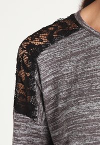 Maglione grigio con un corpo a maglia texturizzata e dettagli in pizzo nero sulle spalle, caratterizzato da una vestibilità ampia e un collo a coste.