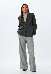 Blazer gris à double boutonnage avec un col à cran, associé à un pantalon gris et blanc à carreaux, ample ; texture de tissu lisse.