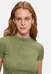 Groen geribbelde T-shirt met korte mouwen en een aansluitende pasvorm. Draagt een gouden ketting met een kleine hanger. Zachte, gestructureerde stof.