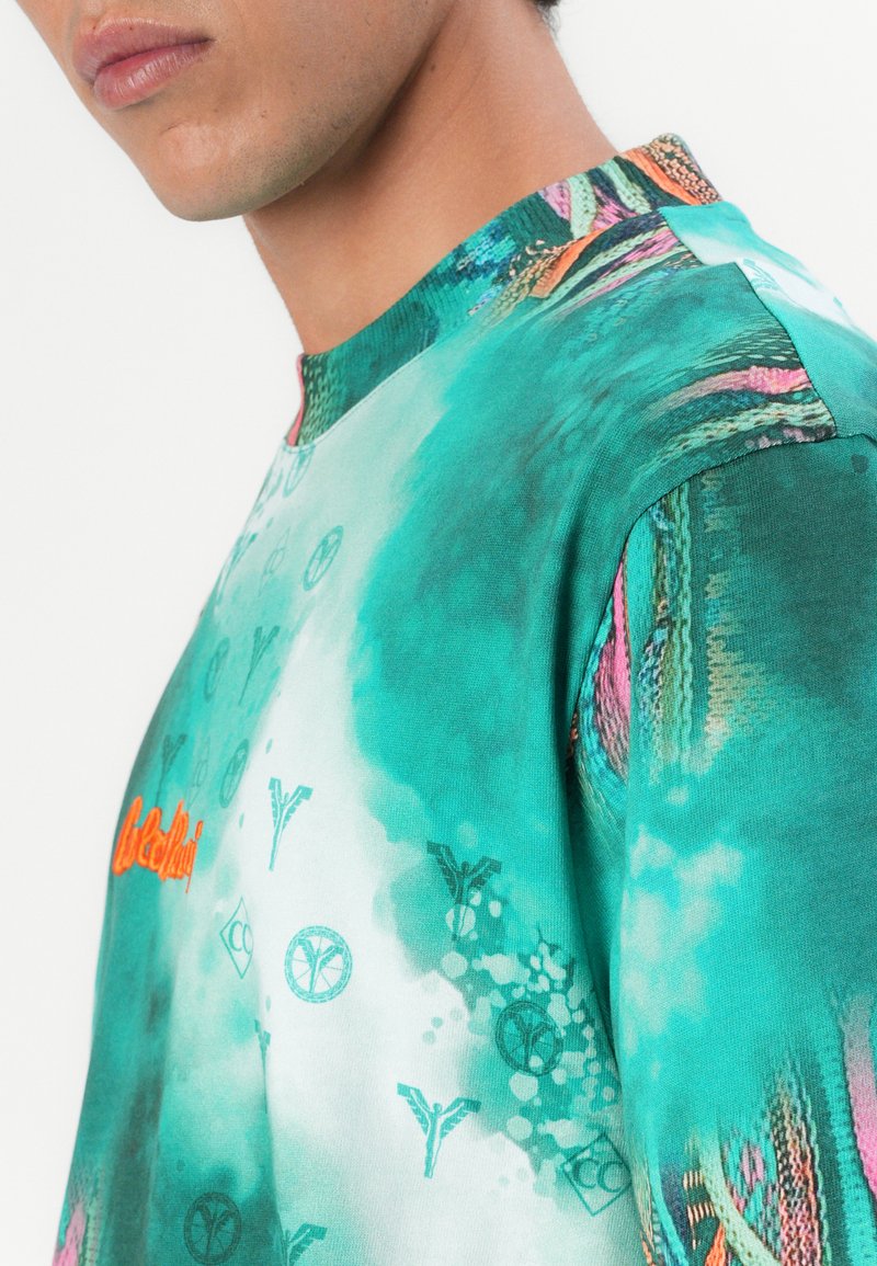 Mintgrüner Pullover mit Rundhalsausschnitt und aufwendigen Mustern in verschiedenen Farbtönen. Auffälliges oranges Logoakzent auf der Brust.