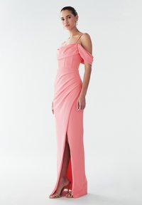Dolga roza obleka z rokavi, ki segajo čez ramena, oprijetim zgornjim delom in stranskim razporkom. Gladek material z detajlom drobnih gub; kombinirana z nagubanimi visokimi petami v bež barvi.