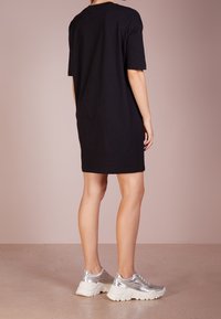 Černé šaty tričkového střihu s krátkými rukávy, volným střihem a kulatým výstřihem, kombinované se stříbrnými teniskami s robustní bílou podrážkou.