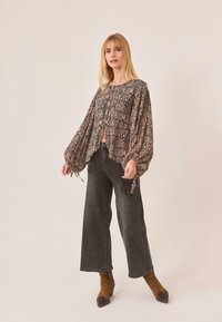 Blusa estampada con mangas largas y vaporosas, que presenta una mezcla de colores terrosos y diseños intrincados, combinada con unos jeans oscuros de cintura alta.