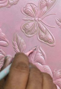 Roze reliëfontwerp met een vlinder en bladeren. Een hand houdt een penseel vast om details toe te voegen. De textuur is glad met verheven patronen.