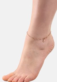 Primer plano de un pie descalzo que lleva un delicado tobillo de oro rosa con un pequeño colgante de corazón sobre un fondo blanco liso.