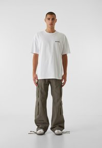 Biele oversized tričko s malým čiernym logom, skombinované s olivovozelenými nohavicami cargo s viacerými vreckami a rovnými nohavicami.