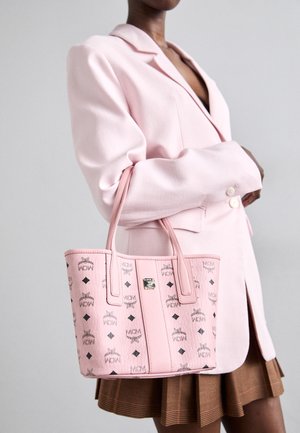 Bolso tote de cuero rosa con una superficie texturizada que presenta un patrón de logotipos repetidos y acentos en negro en forma de diamante. Las asas son estructuradas y cosidas.
