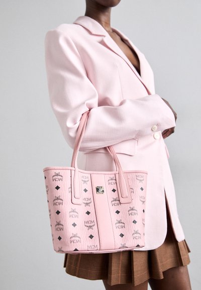 Sac fourre-tout en cuir rose avec une surface texturée présentant un motif de logo répété et des accents en diamants noirs. Les poignées sont structurées et cousues.