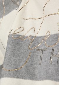 Baumwollmischschal mit abwechselnden grauen und cremefarbenen Streifen, verziert mit goldfarbenen, mit Nieten versehenen Buchstaben und einer weichen Textur.