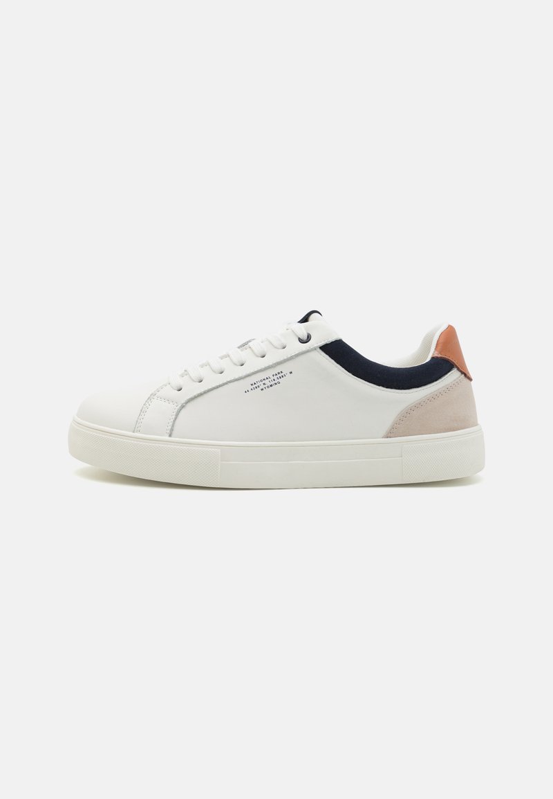 White leather sneakers with a low-top design, navy blue fabric accent on the collar, and a light pink suede heel tab. Rubber sole.
