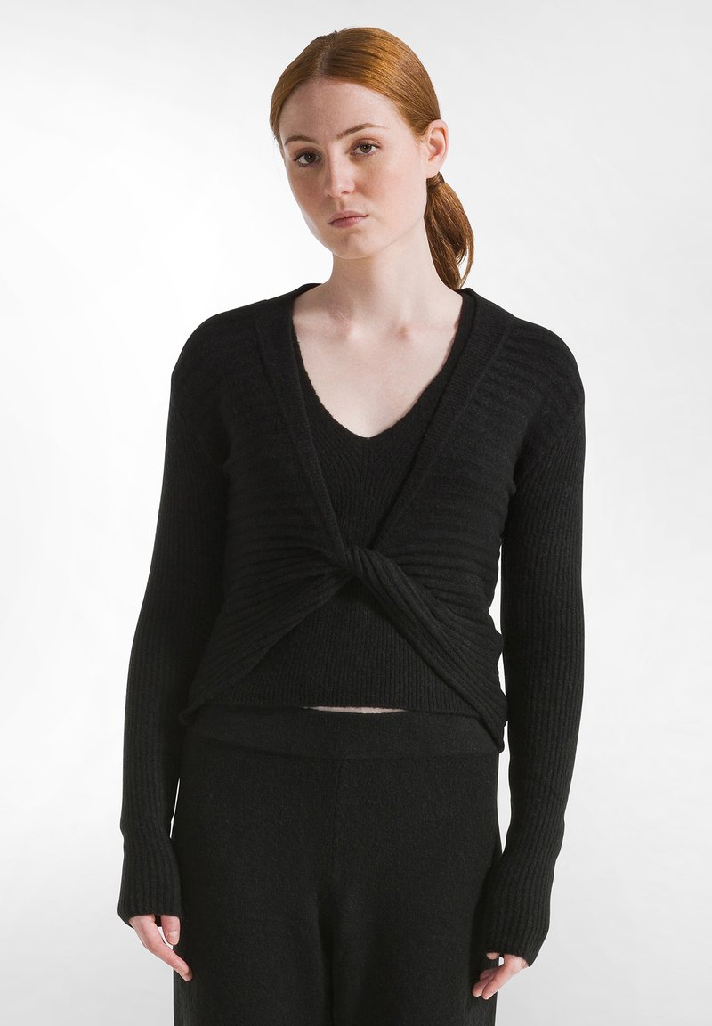 Schwarzer, gerippter Strickpullover mit einer verdrehten Vorderseite. Verfügt über lange Ärmel mit Daumenlöchern. Weiche Textur, tiefer V-Ausschnitt. Eng an der Taille.