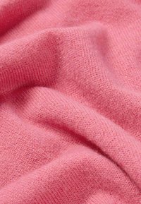 Roze gebreide stof met een zachte, gestructureerde afwerking en zichtbare ribbels en fijne vezels, die in zachte plooien valt.