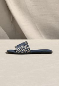 Πλατφόρμα σανδάλι με μπλε σόλα και λουράκι που φέρει γεωμετρικό λουλουδάτο μοτίβο σε μπεζ, μπλε και καφέ αποχρώσεις σε ουδέτερο φόντο.