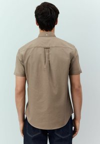 Camisa de mangas cortas de color beige con cuello puntiagudo, pliegue en la parte central de la espalda y dobladillo redondeado. Fabricada con una suave mezcla de algodón texturizado.
