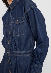 Denimjacke mit knöpfbarem Frontverschluss, zwei Brusttaschen und einem taillierten Zustand. Sie hat die dunkelblaue Farbe und kontrastierende Nähte.