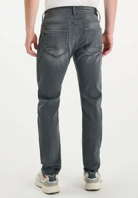 Jeans in denim grigio con una vestibilità dritta, dotati di due tasche posteriori e un leggero sbiadimento. Indossati con scarpe sportive di colore chiaro.