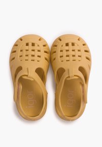 Gelbe Kunststoffsandalen mit einem geflochtenen Design, offenen Seiten und Fesselriemen. Strukturiert Oberfläche, entworfen für Atmungsaktivität und Komfort.