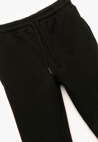 Zwarte sweatpants van zachte stof met een elastische tailleband. Voorzien van een trekkoord met bijpassende zwarte aglets. Eenvoudig ontwerp.