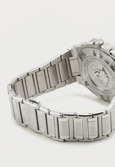 Ασημένιο μπρασελέ από ανοξείδωτο ατσάλι και πίσω κάσα ρολογιού που παρουσιάζουν χαραγμένο έμβλημα λέοντα και κείμενο πάνω σε απλό λευκό φόντο.