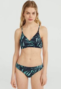 Naine mudel tumesinises ujumistrikoo, millel on rohelised lehepildid, seisab heleda ühtlase tausta ees, silmad otse ette vaadates neutraalse ilmega.