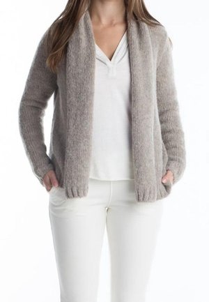 Woman wearing a light gray fuzzy cardigan over a white V-neck shirt and white pants, with hands in cardigan pockets.