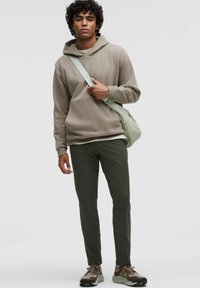 Svijetlosmeđi dukserica s kengurú džepom, maslinasto zeleni hlače i smeđe-zelene tenisice; nosi svijetlozeleni torbicu preko tijela.