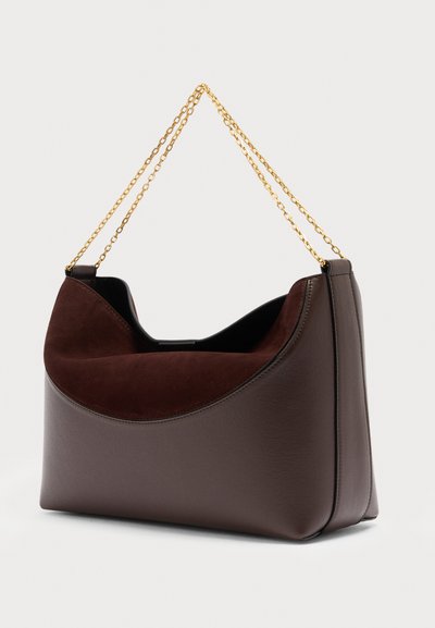 Τσάντα χειρός από σκούρο καφέ δέρμα και σουέτ με χρυσή αλυσίδα ως λουρί, με δομημένο σχέδιο και ανοιχτό επάνω μέρος πάνω σε απλό ανοιχτόφωτο φόντο.