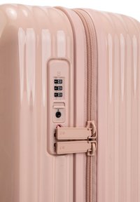 Valigia rigida di colore rosa pastello, con superficie testurizzata, serratura a tre cifre, chiusura a zip e doppie zip per un accesso sicuro.
