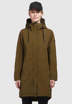 Manteau long marron avec fermeture éclair et capuche ajustable. Présente deux poches latérales et un design simple et fonctionnel. Casquette noire portée.