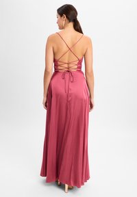 Langes, ärmelloses Kleid aus staubrosa Satin. Besitzt ein überkreuztes Trägerdesign am Rücken und eine gebundene Taille zur Formgebung. Glatte Textur.