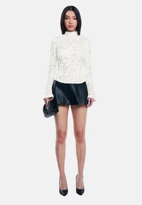 Hvid blondebluse med høj hals og lange ærmer, kombineret med en sort mininederdel i læder. Modellen holder en sort clutch og har sorte højhælede sko på.