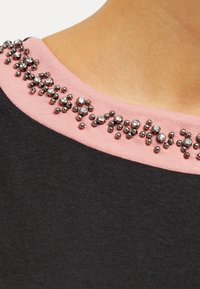 Svart tygtop med en rosa halsringning prydd med dekorativa silver- och klara rhinestones i varierande storlekar.