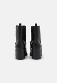 Czarne skórzane botki za kostkę o gładkim wykończeniu, z blokowym obcasem i uchwytem, podkreślające elegancki, minimalistyczny design.