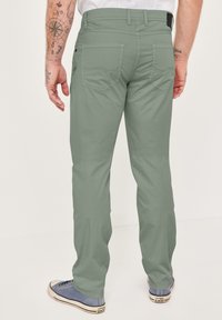 Hellgrüne Hose mit geradem Schnitt. Verfügt über zwei Gesäßtaschen mit abgerundeten Klappen und einer glatten Stofftextur. Kombiniert mit blauen Sneakern.