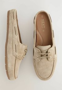 Beige suede loafers with a smooth textured surface, rounded toe, contrasting brown rubber sole, and decorative lacing and eyelets.