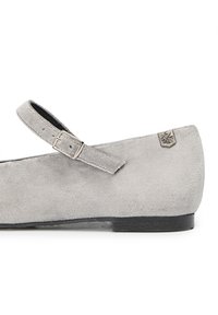 Zapato plano de ante gris con punta redonda, tira en el tobillo con un hebilla de metal y un pequeño logo en el lado exterior.