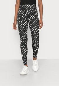 Leggings pretos em estilo ajustado, com um padrão de formas de crescente brancas, feitos de material elástico, combinados com ténis brancos.