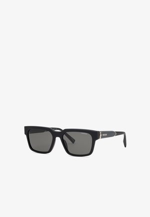 Lunettes de soleil rectangulaires noires avec des verres foncés et des accents argentés sur les branches, marquées "Chopard" dans le coin de la monture.
