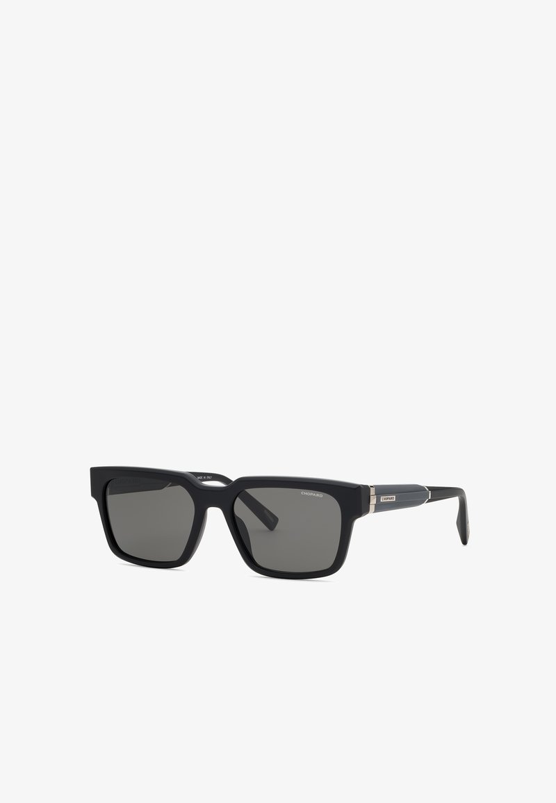 Lunettes de soleil rectangulaires noires avec des verres foncés et des accents argentés sur les branches, marquées "Chopard" dans le coin de la monture.