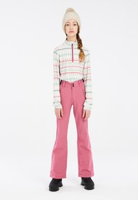 Pull à manches longues, zippé, avec un motif géométrique dans des couleurs pastel, associé à un pantalon de neige rose, évasé, et des bottes noires et robustes.