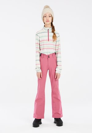 Lange mouwen, ritspull met een geometrisch patroon in pastelkleuren, gecombineerd met roze, flared sneeuwbroeken en zwarte, stevige laarzen.